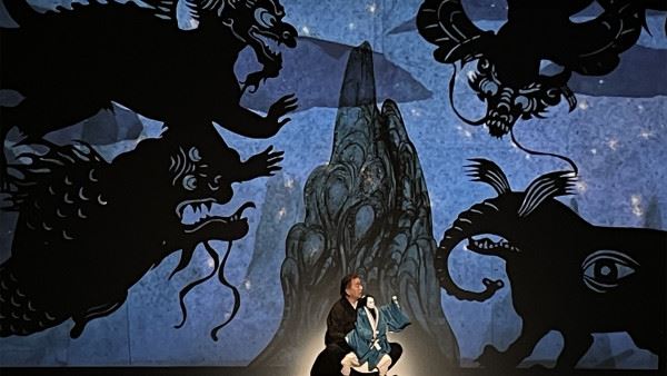 Photo of a performer and puppet against a dramatic background.